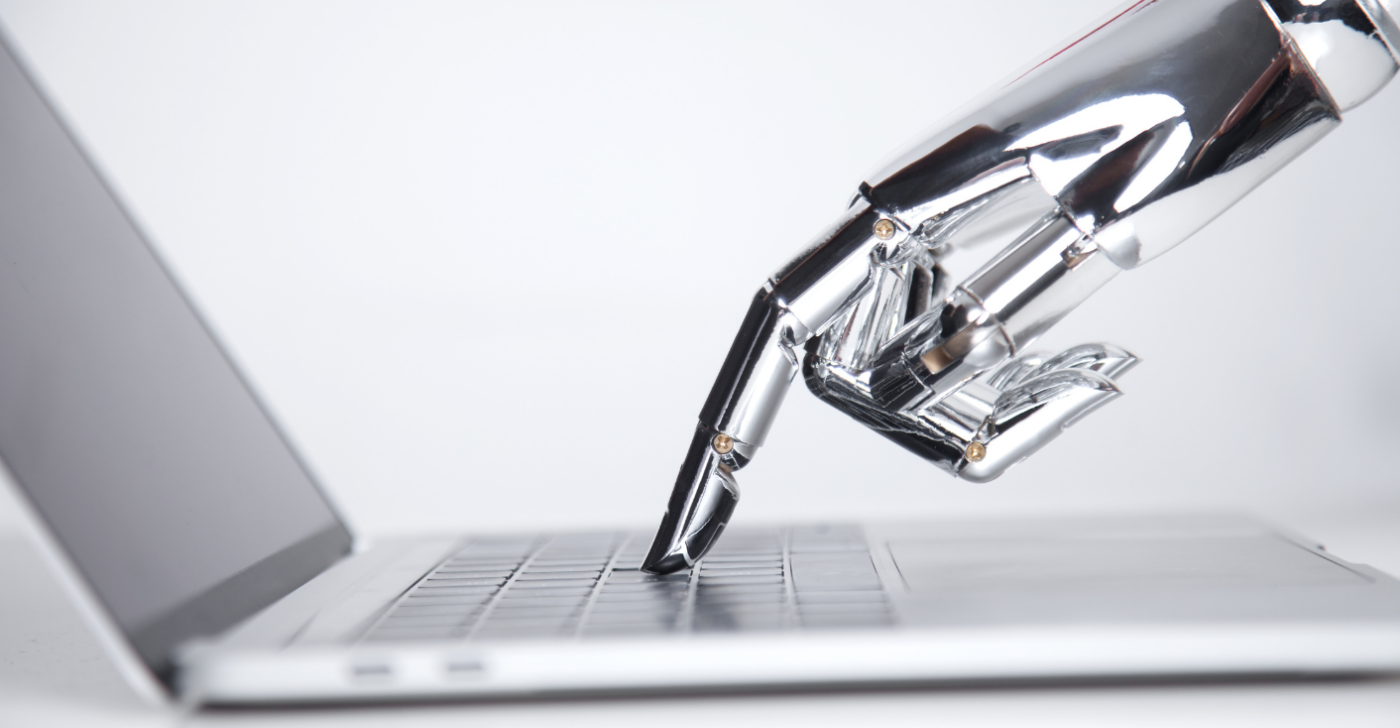 A robot hand it typing on a computer to symbolize generative AI content creation.