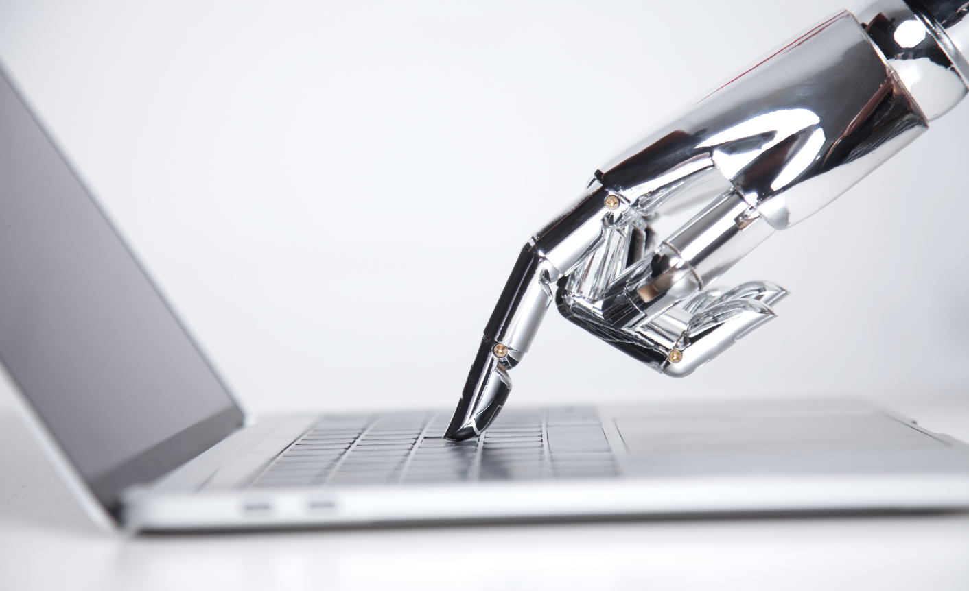 A robot hand it typing on a computer to symbolize generative AI content creation.