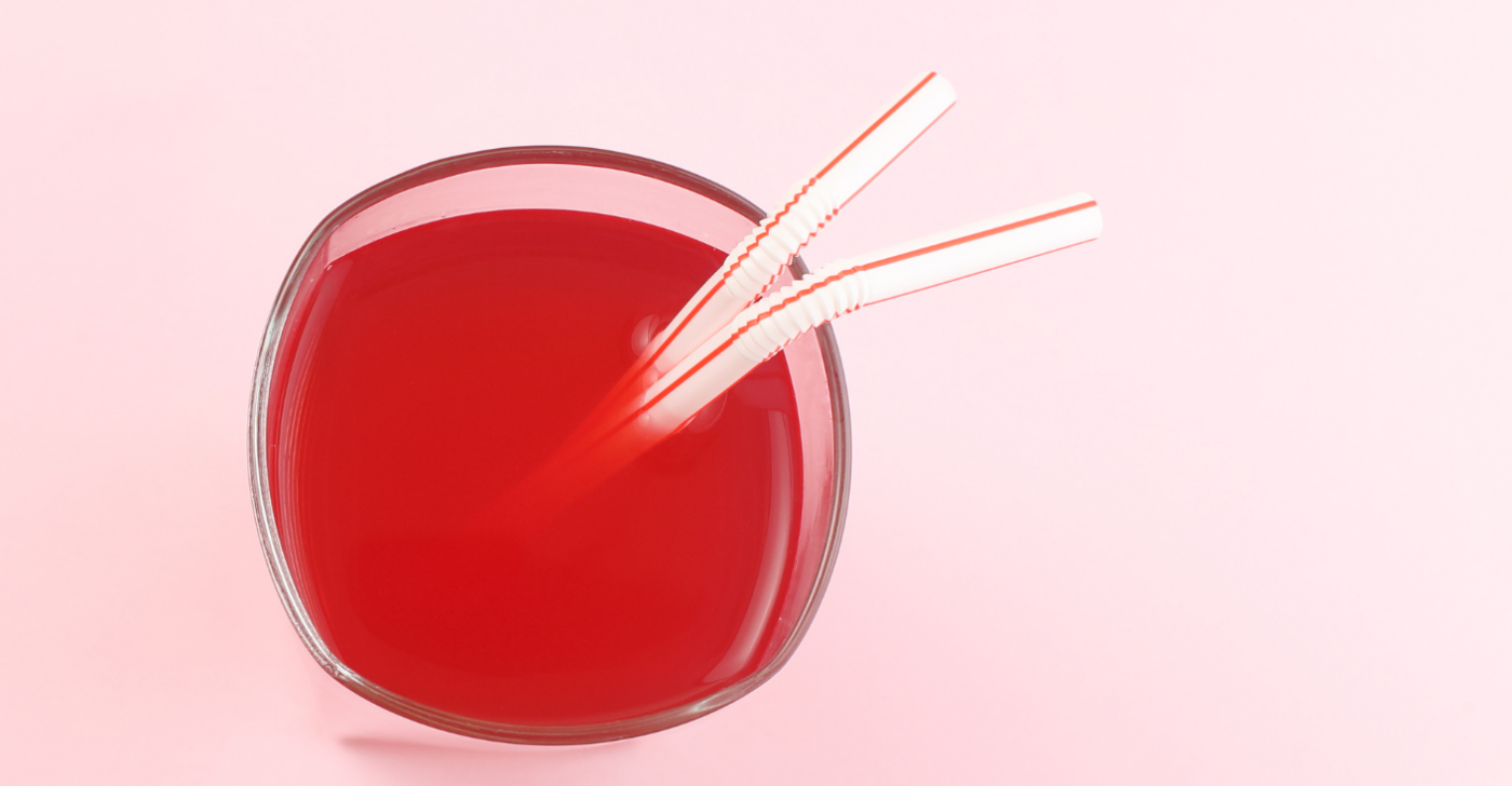 On a light pink background a class of red juice has two straws coming out of it to symbolize how to merge two brands.