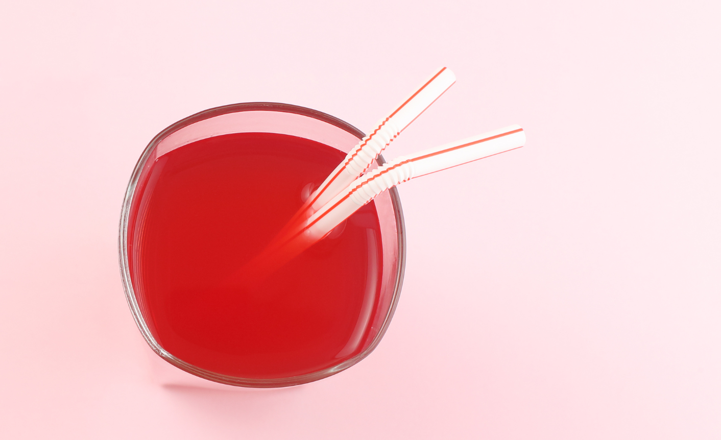 On a light pink background a class of red juice has two straws coming out of it to symbolize how to merge two brands.