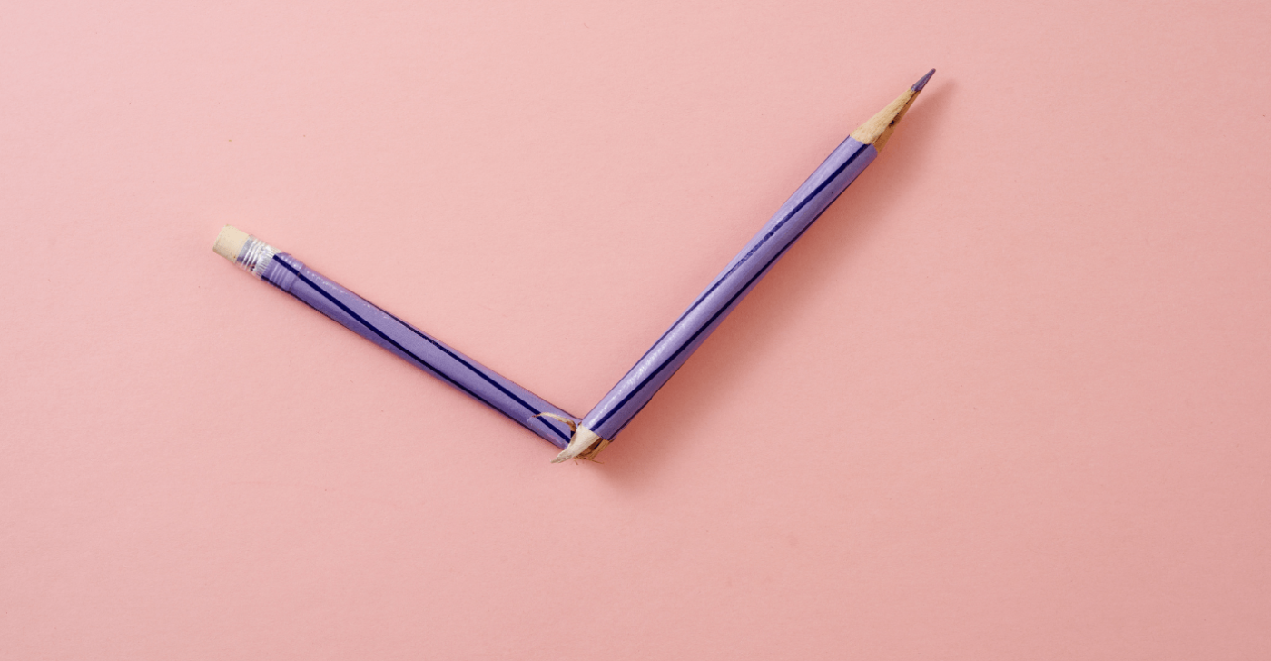 A purple pencil is broken in half on a pink background - to symbolize writing mistakes.