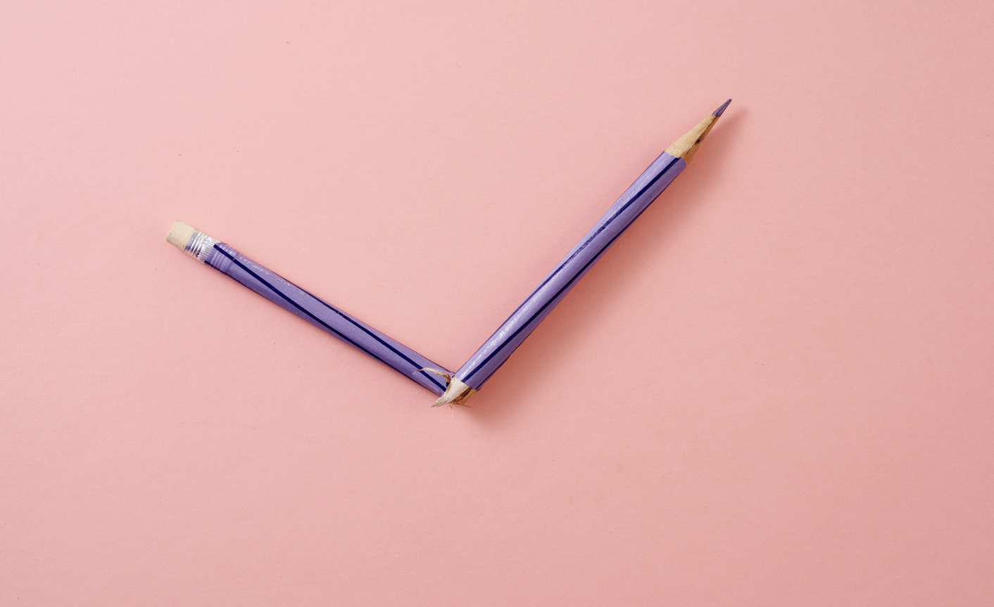 A purple pencil is broken in half on a pink background - to symbolize writing mistakes.