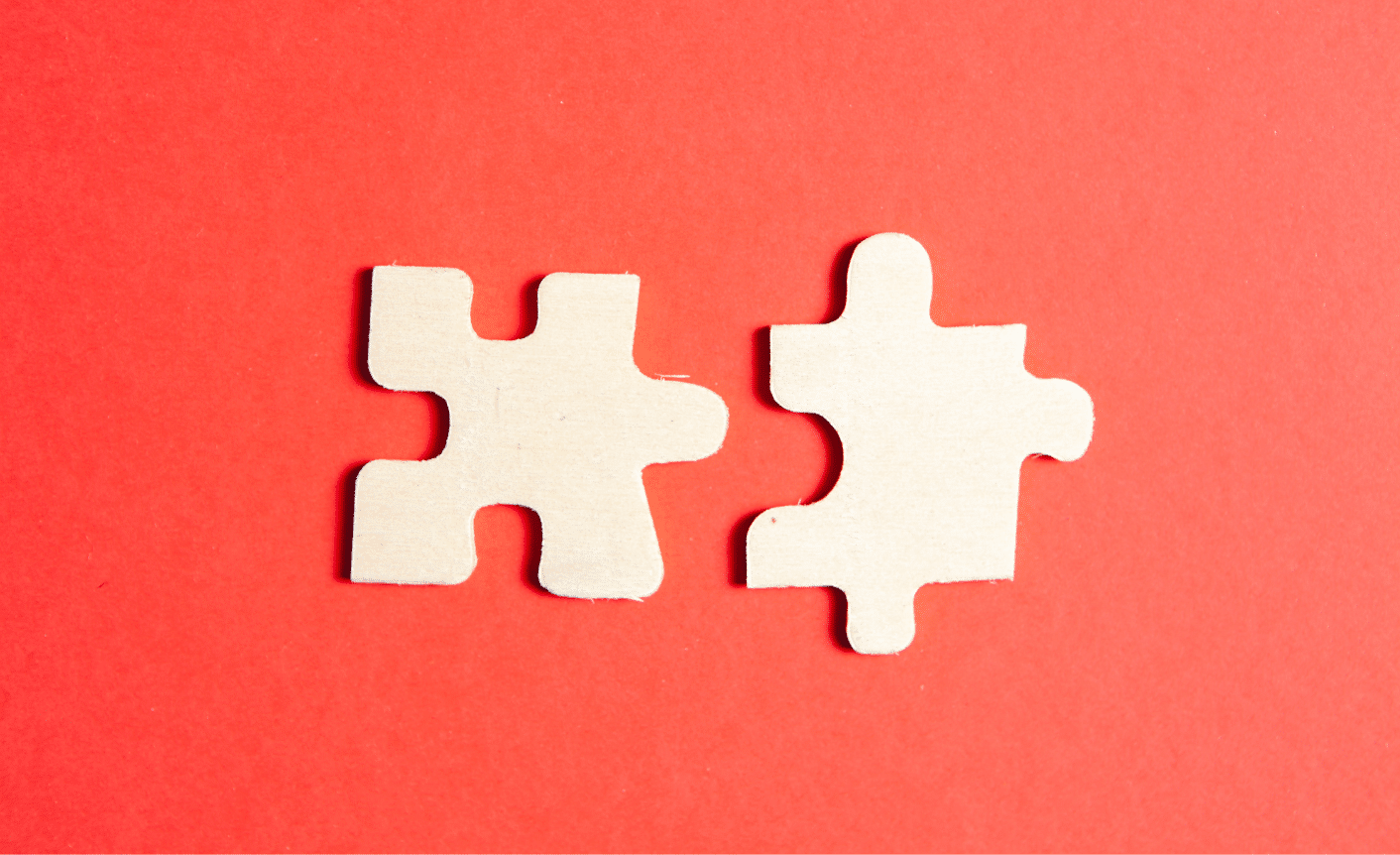 MA-blog Two white puzzle pieces on a red background to symbolize the unification of two different content operations after a merger and acquisition.
