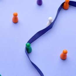 Ein blaues Satin-Band dient als Orientierung für bunte Holzfiguren und steht symbolisch für das Schreiben nach Vorgaben.